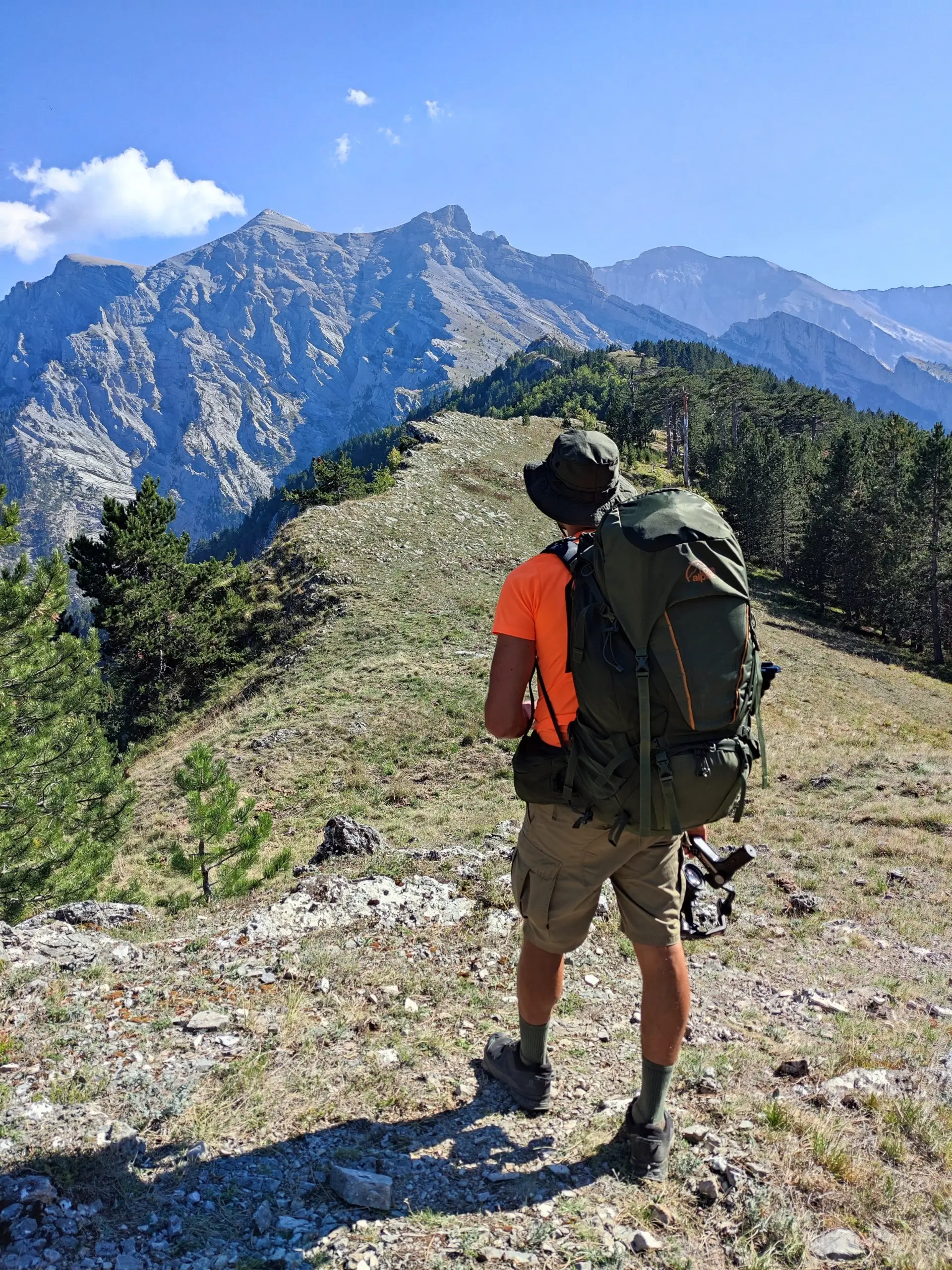 Hiker with a large backpack standing on a mountain ridge overlooking the majestic peaks of Mount Olympus in Greece