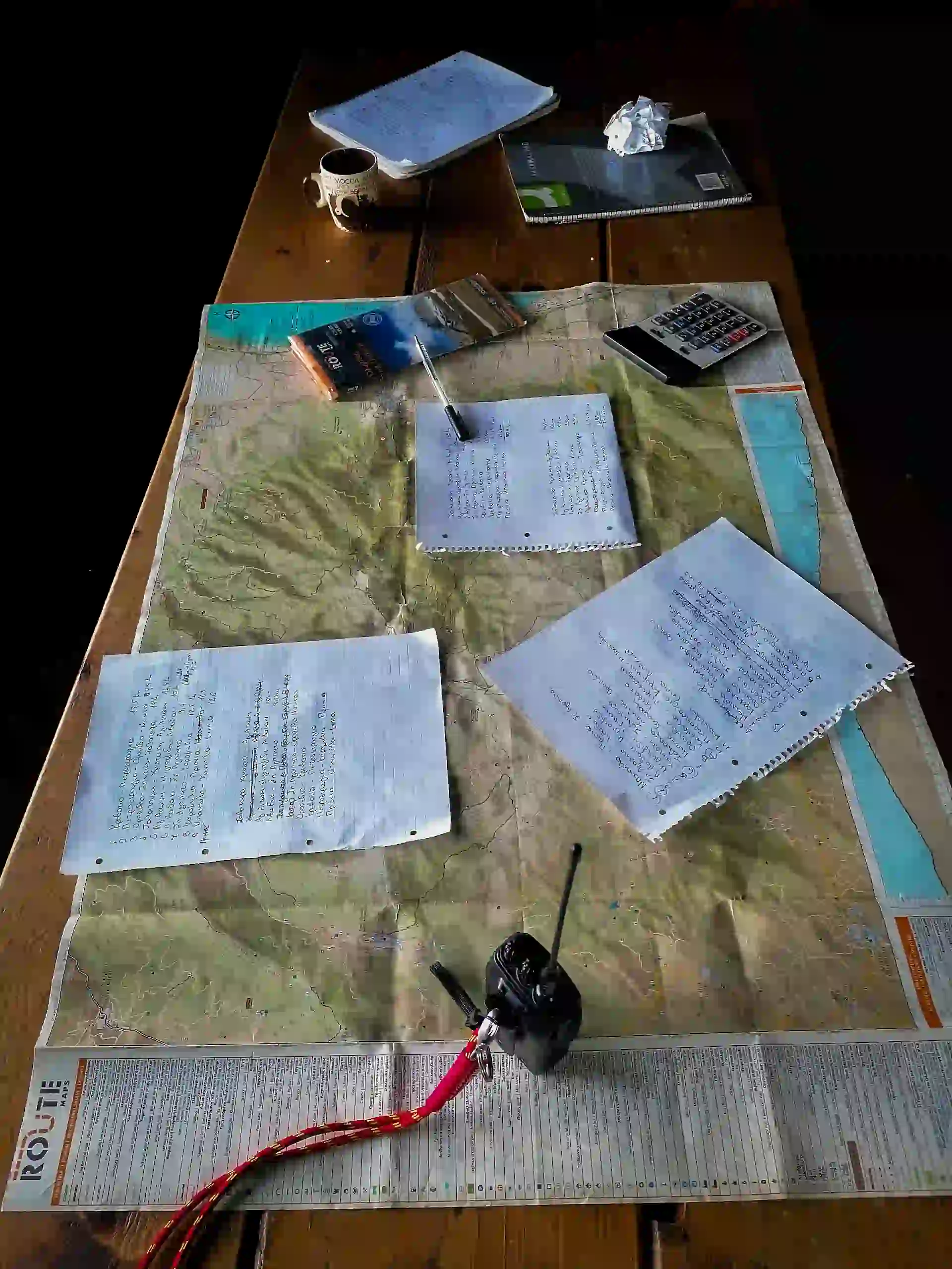 A topographic map of Mount Olympus spread on a wooden table with handwritten notes and planning equipment for a professional hiking expedition.